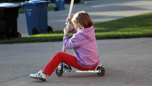 Young girl riding a scooter on a paved driveway.