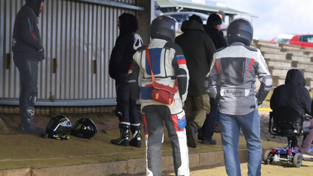 People in racing suits stand near helmets
